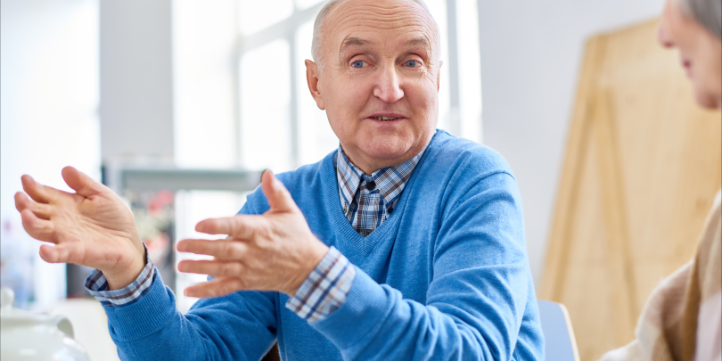 A man with a blue sweater talking with another person.